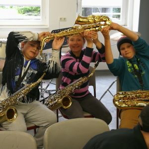 Drei Schüler_innen zeigen ein das neue Saxofon